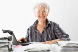 een wat oudere vrouw een nette donker blauwe broek aan en aan het werk op een laptop dit is voor de Vacature avond conciërge